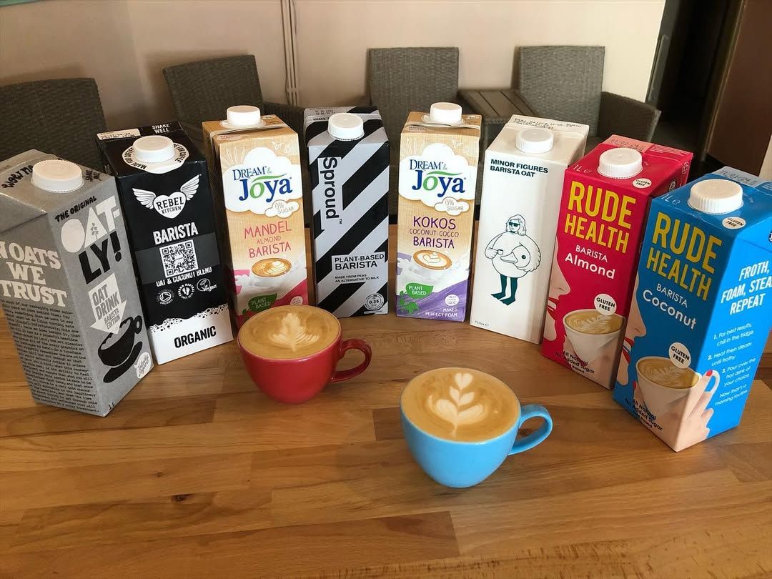 Dvě cappuccina s latte art před řadou krabic rostlinných mlék
